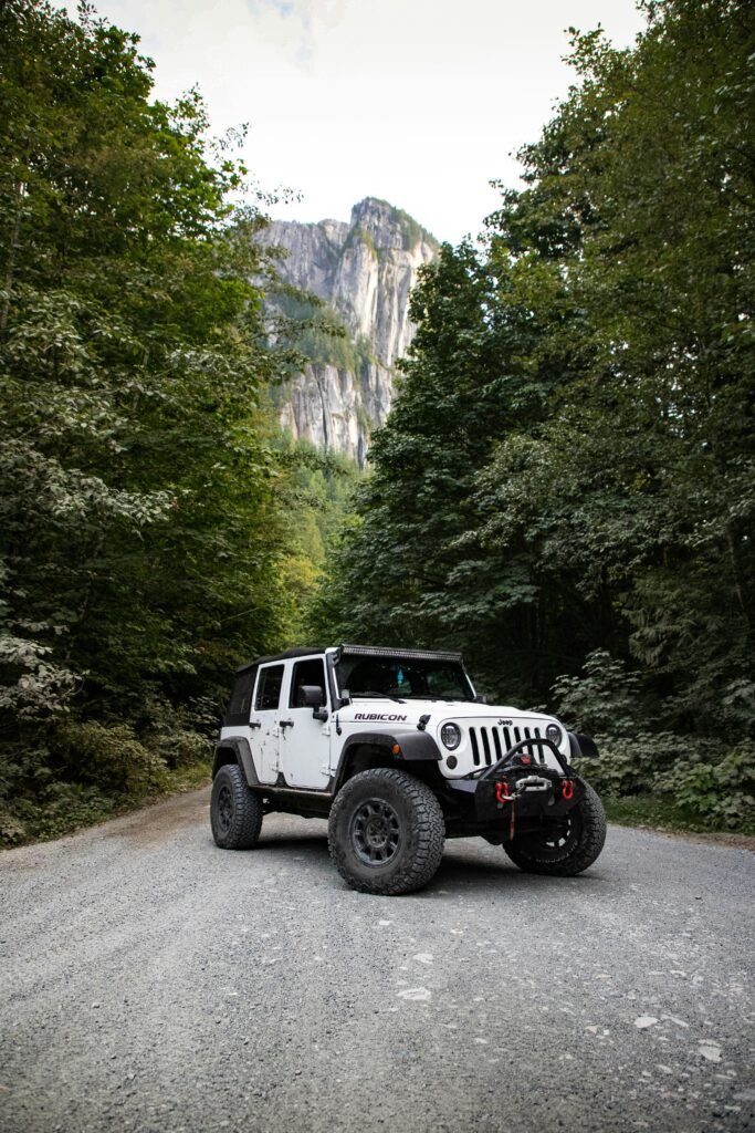 pexels-photo-2882234-2882234 A rugged Jeep Wrangler on a gravel road surrounded by lush forest and towering mountains.